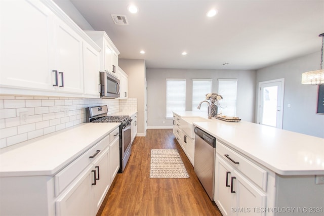 kitchen featuring stainless steel appliances, white cabinetry, dark wood-type flooring, and an island with sink