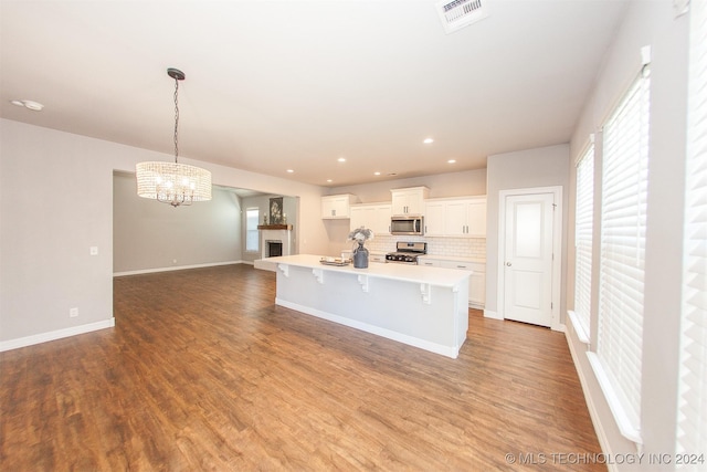 kitchen featuring a kitchen bar, stainless steel appliances, a center island with sink, hardwood / wood-style floors, and white cabinetry