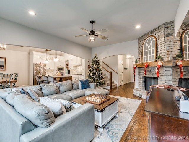 living room featuring a stone fireplace, ceiling fan, and dark wood-type flooring