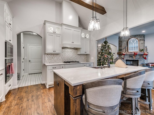 kitchen with stainless steel appliances, a kitchen island with sink, sink, high vaulted ceiling, and hanging light fixtures