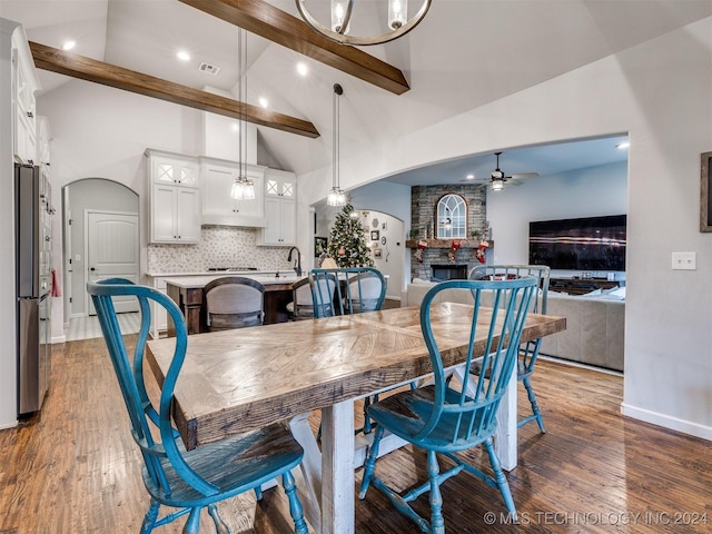 dining area featuring beam ceiling, ceiling fan, dark wood-type flooring, high vaulted ceiling, and a fireplace