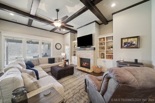 living room featuring beamed ceiling, wood-type flooring, a stone fireplace, and ceiling fan