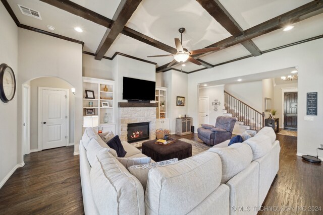 living room with ceiling fan with notable chandelier, beam ceiling, dark hardwood / wood-style flooring, and a stone fireplace