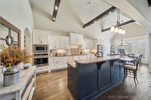 kitchen with white cabinets, a center island with sink, beamed ceiling, and appliances with stainless steel finishes