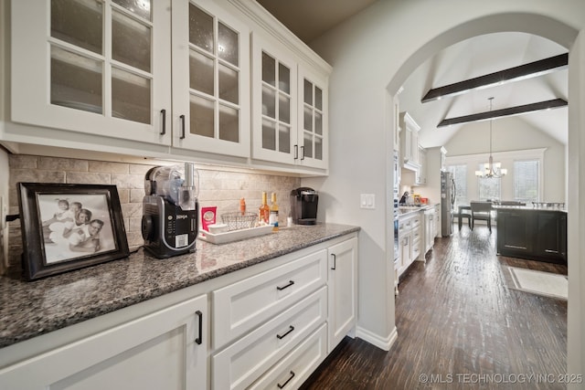 kitchen with dark wood-style flooring, decorative backsplash, arched walkways, stone countertops, and freestanding refrigerator