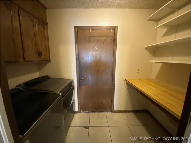 clothes washing area featuring cabinets, light tile patterned floors, a textured ceiling, and washer and clothes dryer