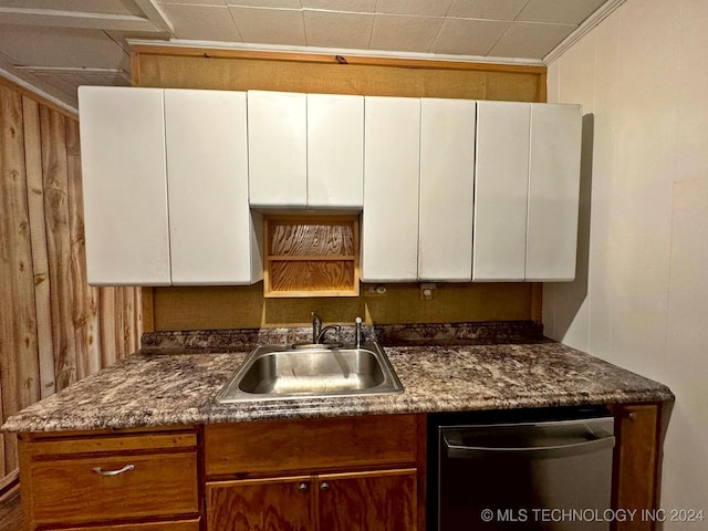 kitchen with dishwasher, wood walls, white cabinetry, and sink