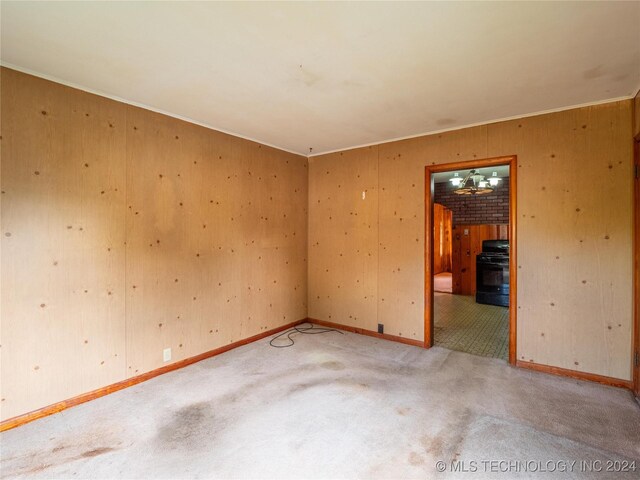 empty room with light colored carpet, ornamental molding, and wooden walls