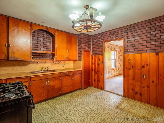 kitchen with sink, brick wall, a notable chandelier, wooden walls, and black range