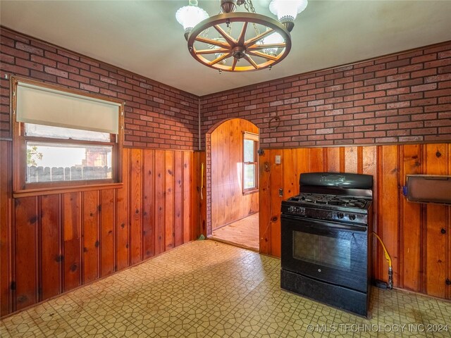 kitchen featuring wood walls, black range with gas cooktop, and brick wall