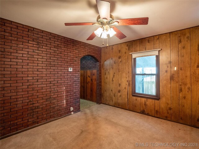 spare room featuring wooden walls, light colored carpet, brick wall, and ceiling fan