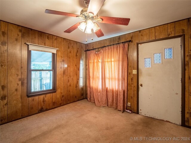 carpeted spare room featuring ceiling fan and wooden walls
