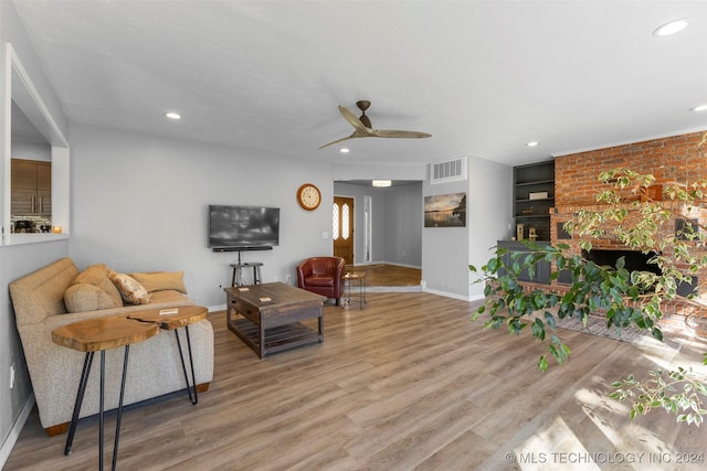 living room featuring ceiling fan, light hardwood / wood-style flooring, and a brick fireplace