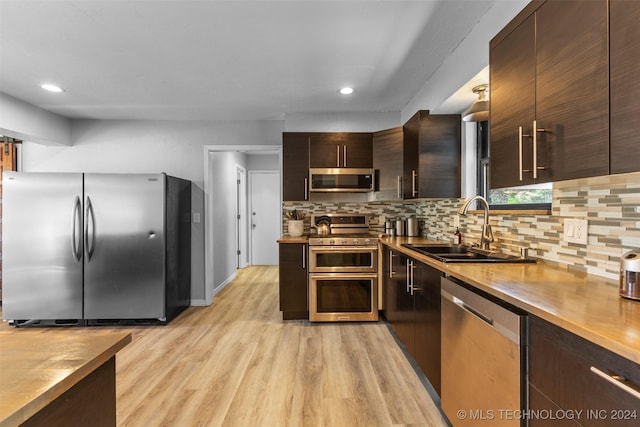 kitchen with dark brown cabinetry, sink, backsplash, appliances with stainless steel finishes, and light wood-type flooring