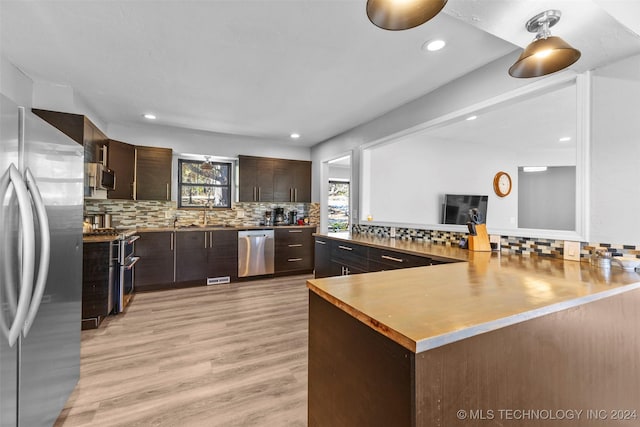 kitchen with backsplash, light wood-type flooring, appliances with stainless steel finishes, dark brown cabinets, and kitchen peninsula