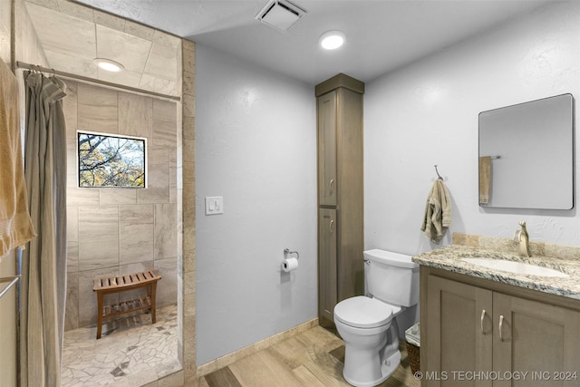 bathroom featuring tiled shower, toilet, vanity, and hardwood / wood-style flooring