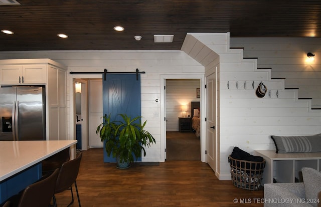 kitchen featuring white cabinets, stainless steel refrigerator with ice dispenser, a barn door, and wood walls