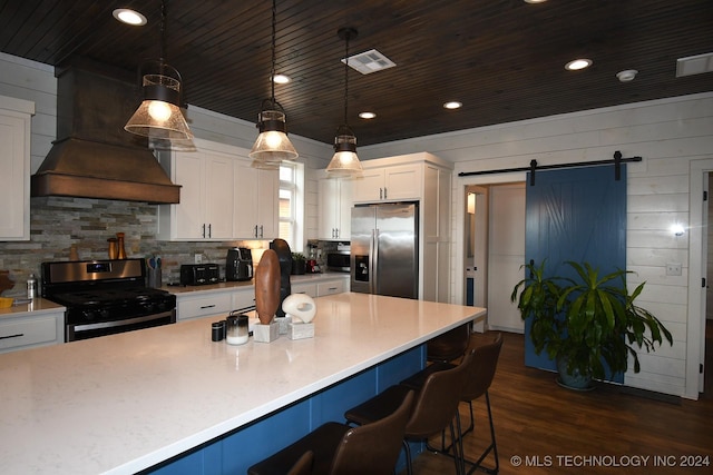 kitchen with pendant lighting, custom exhaust hood, a barn door, a kitchen bar, and stainless steel appliances