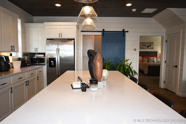 kitchen featuring wood walls, hanging light fixtures, a barn door, appliances with stainless steel finishes, and white cabinetry