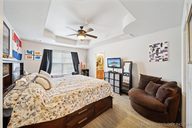 bedroom with a tray ceiling, ensuite bath, and ceiling fan