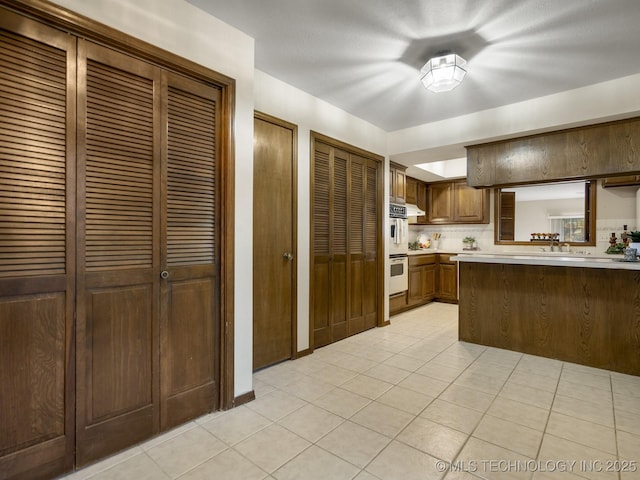 kitchen featuring kitchen peninsula, light tile patterned floors, decorative backsplash, double oven, and sink