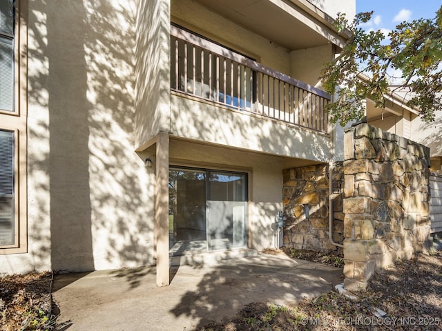 rear view of house featuring stone siding, a balcony, a patio area, and stucco siding