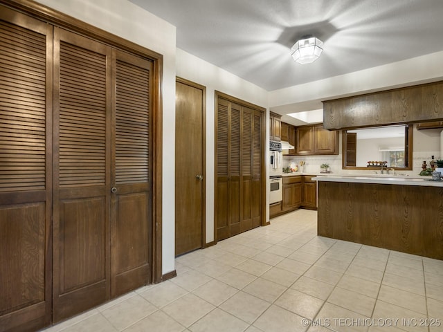 kitchen with light tile patterned flooring, double oven, light countertops, a sink, and backsplash