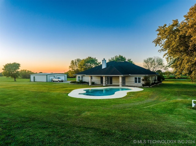 back house at dusk with an outbuilding, a garage, and a lawn