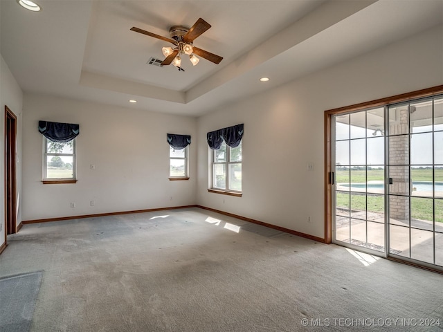 unfurnished room featuring a raised ceiling, ceiling fan, and light carpet