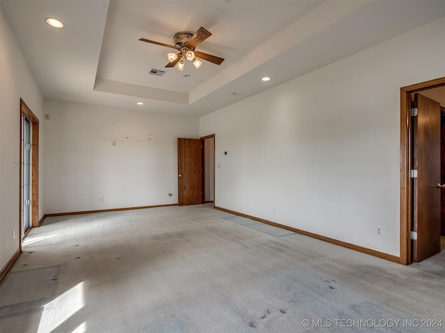 carpeted empty room with a raised ceiling and ceiling fan