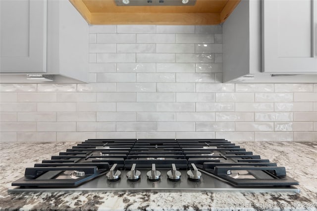 details with backsplash, white cabinetry, stainless steel gas stovetop, and light stone counters