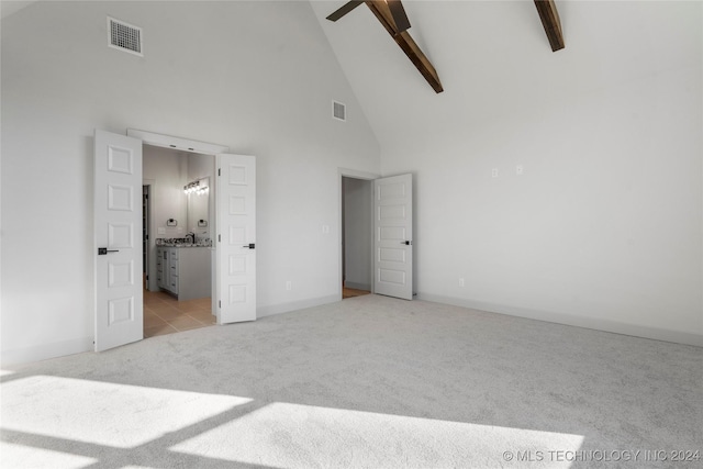 unfurnished bedroom featuring light colored carpet, ceiling fan, beam ceiling, high vaulted ceiling, and connected bathroom