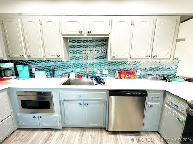 kitchen with backsplash, sink, stainless steel dishwasher, light wood-type flooring, and white cabinetry