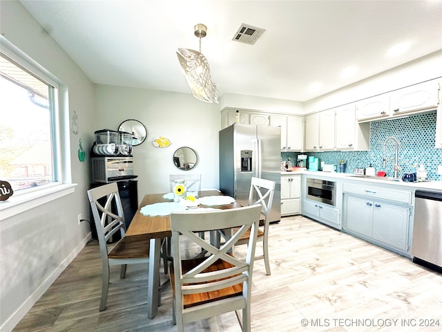 kitchen featuring sink, hanging light fixtures, tasteful backsplash, light hardwood / wood-style floors, and stainless steel appliances