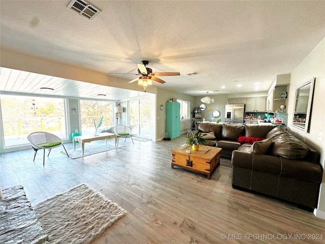 living room featuring ceiling fan, a textured ceiling, and light wood-type flooring