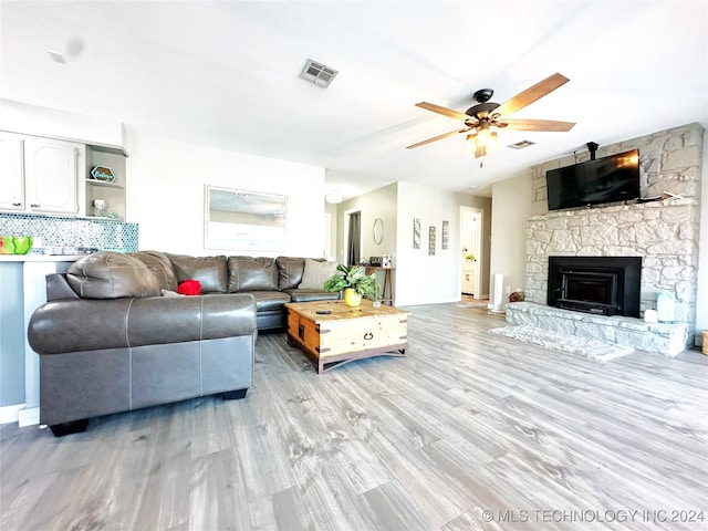 living room featuring light wood-type flooring, a stone fireplace, and ceiling fan