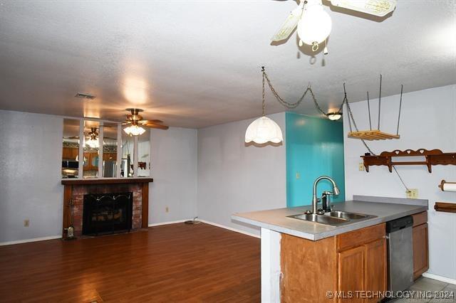 kitchen with sink, dark wood-type flooring, stainless steel dishwasher, decorative light fixtures, and a fireplace