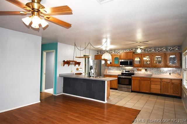 kitchen featuring ceiling fan, tasteful backsplash, kitchen peninsula, hardwood / wood-style floors, and appliances with stainless steel finishes