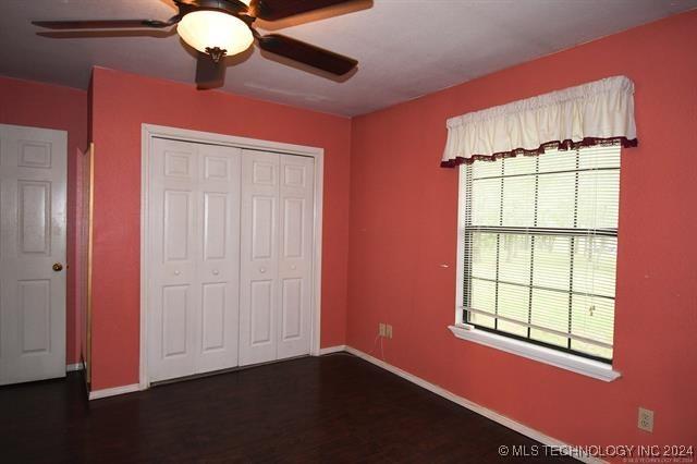 unfurnished bedroom featuring multiple windows, ceiling fan, a closet, and dark hardwood / wood-style floors