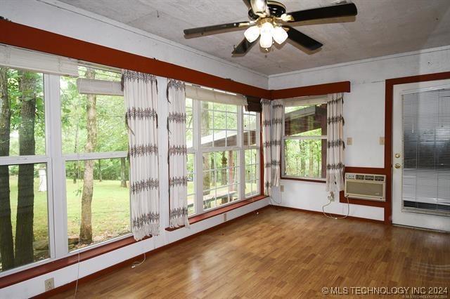 unfurnished sunroom with a wall unit AC and ceiling fan