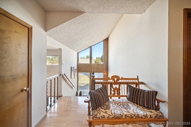 hall featuring lofted ceiling, a textured ceiling, and light hardwood / wood-style flooring