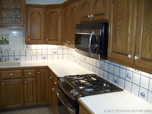 kitchen featuring decorative backsplash, sink, black range oven, and light tile patterned floors