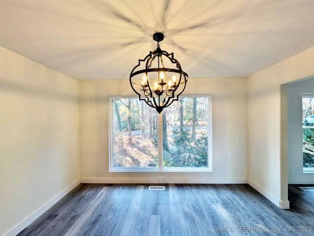 unfurnished dining area featuring a notable chandelier, dark hardwood / wood-style floors, and a wealth of natural light