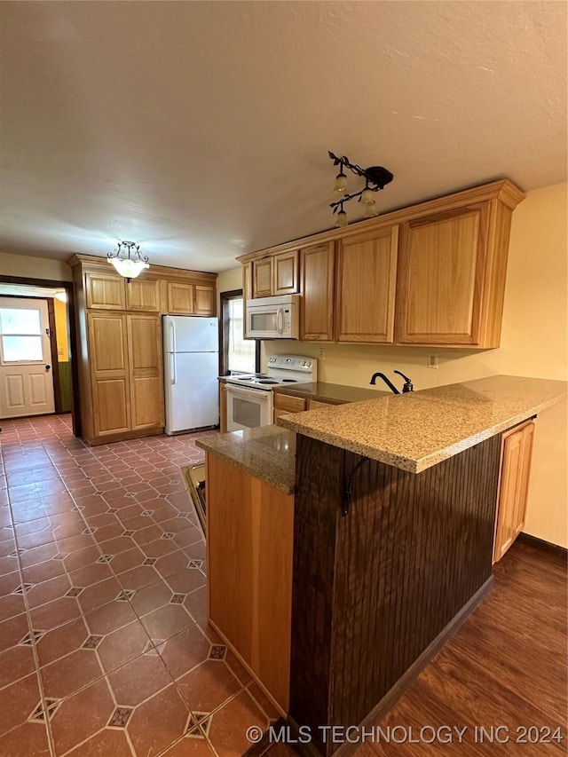 kitchen with a kitchen bar, kitchen peninsula, dark wood-type flooring, and white appliances