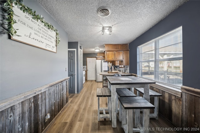 dining area featuring a textured ceiling, light hardwood / wood-style floors, and wooden walls