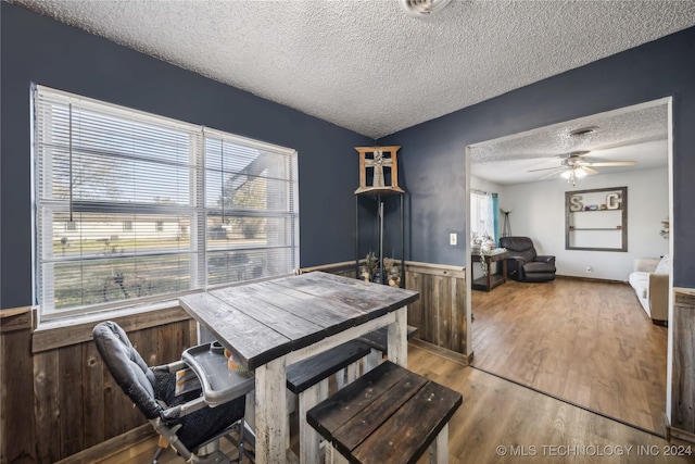 dining room featuring ceiling fan, wood walls, light hardwood / wood-style floors, and a textured ceiling