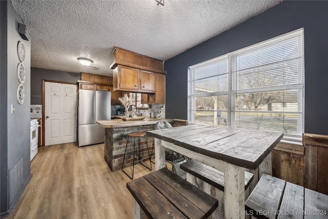 kitchen with stainless steel refrigerator, decorative backsplash, a textured ceiling, and light wood-type flooring