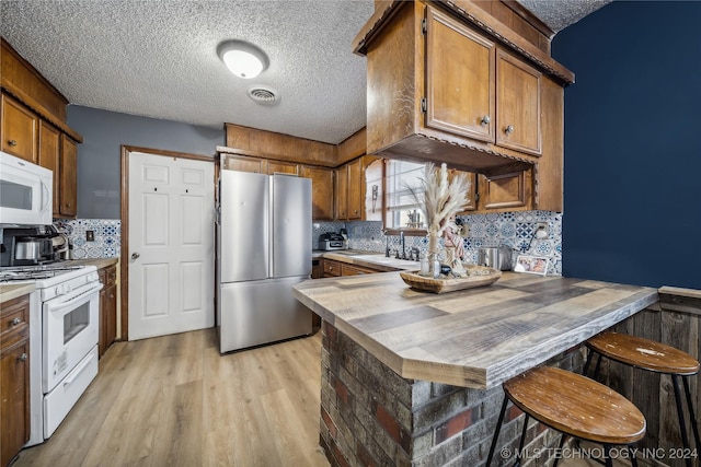 kitchen with white appliances, a textured ceiling, tasteful backsplash, light hardwood / wood-style floors, and a breakfast bar area