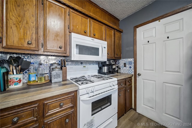 kitchen with decorative backsplash, a textured ceiling, white appliances, and hardwood / wood-style floors