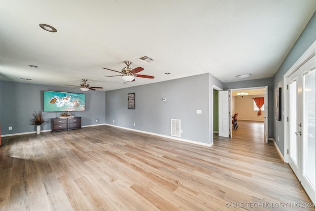 unfurnished living room with ceiling fan with notable chandelier and light hardwood / wood-style floors